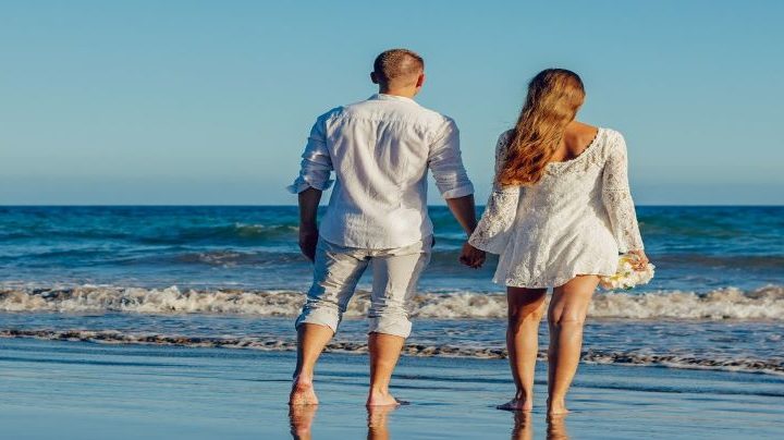 Pareja cogidos de la mano, de pie a la orilla del mar